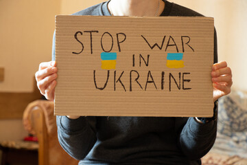 Stop the war in Ukraine written on a sign that a woman holds in her hands from her house in the...