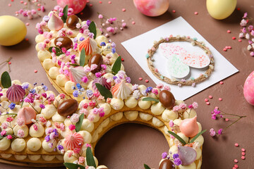 Beautiful cake, painted eggs, flowers and greeting card for Easter celebration on brown background, closeup