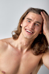 Young handsome shirtless man with long hair showing sexy body over isolated background smiling...