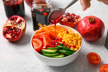 Pouring of pomegranate molasses onto fresh vegetable salad on light background