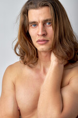 Brooding naked man looking at camera and rubbing neck isolated over white background. Young caucasian guy with long hair posing at camera, looking thoughtful and pacified, calm