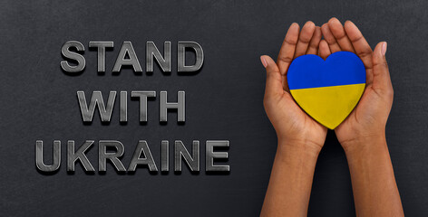 Stand With Ukraine. Woman holding heart painted in colors of Ukrainian flag