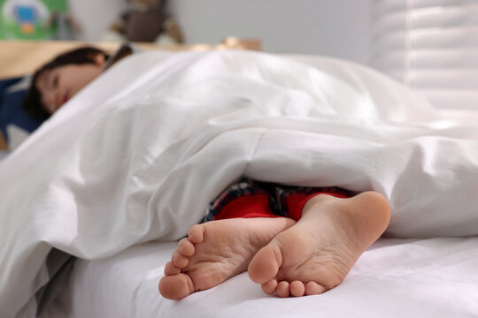 Little boy sleeping in bed at home, focus on feet