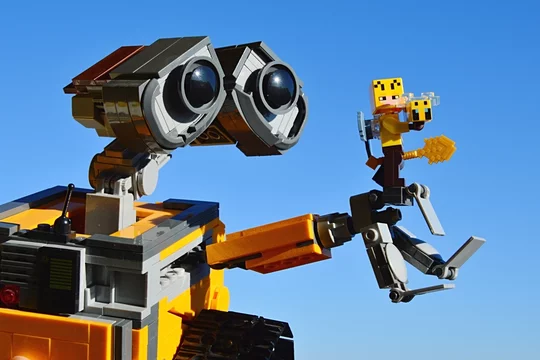 Foto Stock LEGO Wall-E robot from Disney Pixar movie of the same name,  holding LEGO Minecraft Beekeeper with bee and golden shovel on his left  arm, blue spring skies in background.