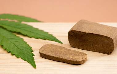 hashish tablet, hashish portion 100 grams, with large marijuana leaf, on wood, brown background