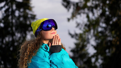 Bright curly girl snowboarder in a yellow-blue suit against the backdrop of a mountain forest.