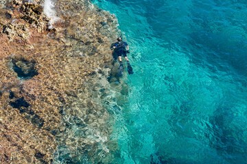 Man in diving suit swims in the sea near coral reef. Pure turquoise water. Top view. Water Activities.