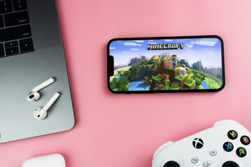 Obraz premium Minecraft mobile game app on the smartphone screen. Pink background with computer, AirPods, video game controller. Rio de Janeiro, RJ, Brazil. March 2022