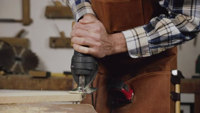 Carpenter is sawing a wood plank with electric jig saw machine in carpentry workshop. Workwood DIY concept. High quality 4k footage