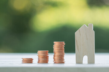 Many gold coins are oriented towards growth and a house model placed on a wooden table. Investing...