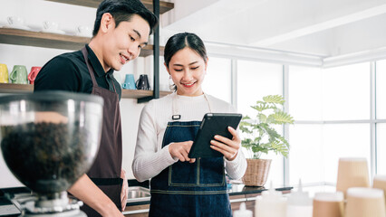 Successful Asian young male and female barista cafe entrepreneur check coffee buy order from a digital tablet. Small business coffee shop owner. Image with copy space.