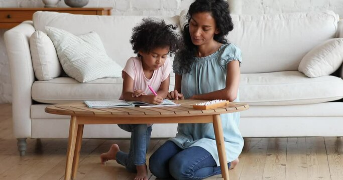 Young Black mommy teach little preschool age daughter to count explain math basics using abacus help do sums in workbook. Smart child girl prepare for school learn mathematics together with mom nanny