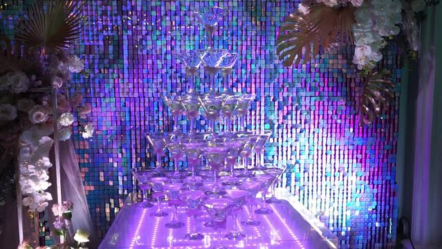 a large pyramid of glasses with an alcoholic cocktail on a neon-lit table in a nightclub, a bartender shows in a bar