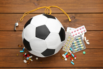Soccer ball, whistle and different pills on wooden table, flat lay. Doping concept