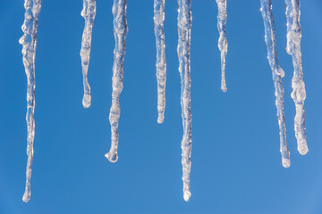 Long icicles on a blue sky background. Ice floes hang from the roof.