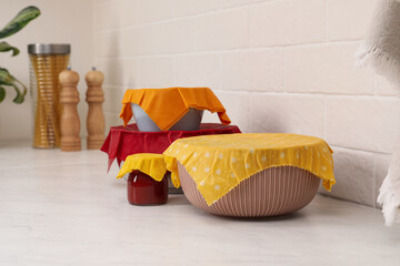Different dishware covered with beeswax food wraps on white table. Space for text