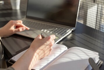 Obraz premium Hands closeup taking notes, writing in business planner at laptop computer at desk.