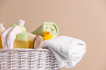 Wicker basket with baby cosmetic products, bath accessories and rubber duck on beige background, closeup