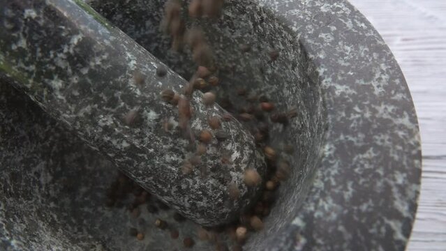 Close-up of the black peppercorns are falling into the grey stone mortar