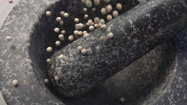 Spicy exotic white peppercorns are falling and bouncing in the grey stone mortar