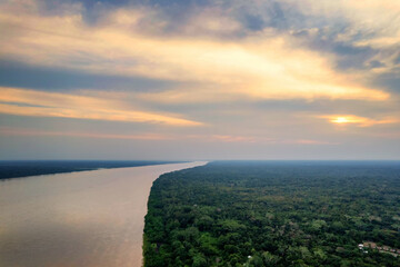 Aerial view of the Amazon River and forest at sunset, with a small village, during the wet season