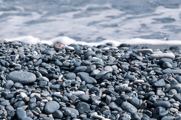 Gray stones and pebbles on the beach in front of  foamy sea water