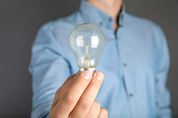 Man holding incandescent light bulb on grey background, closeup