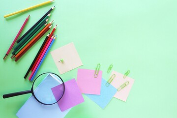 Stationery and an alarm clock, pastel colored paper, on a green background, top view, the concept of learning, education, back to school, holidays