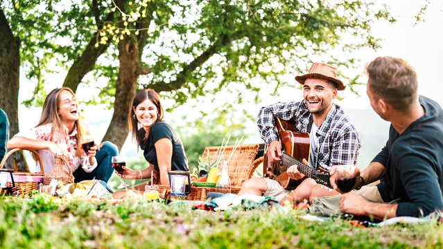 Friends group having fun moment at pic nic playing guitar on sunset - Friendship life style concept with young people enjoying springtime camping together at park location - Bright greenish filter