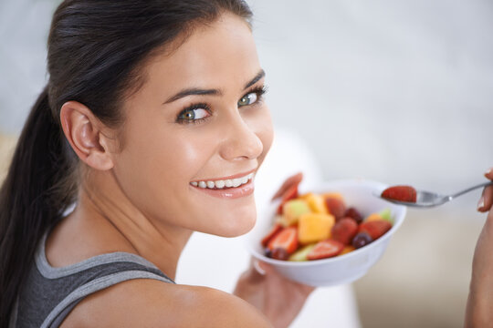 My healthy snack. A young woman eating a bowl of chopped fruit.