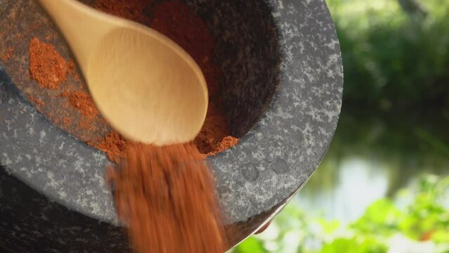Bamboo spoon is taking a mix of spices and peppers from the grey stone mortar