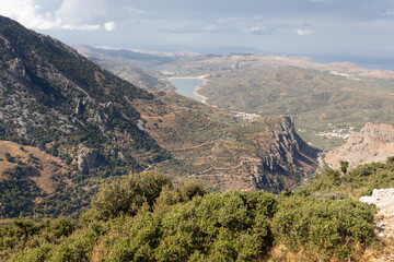 Fototapeta na wymiar Landscape of valley with rocks, bushes, winding road and lake disappearing in haze, Crete, Greece