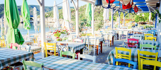 Table restaurant at traditional Greek taverna on the beach. Summer vacation. - obrazy, fototapety, plakaty