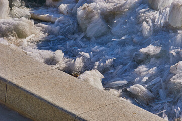 Fragment of a granite embankment of the river in spring with a scattering of fragments of melting ice floes.