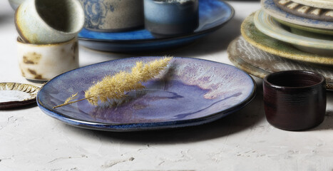 Glazed, ceramic, blue handmade plate with dried flowers on the background of various clay dishes. Close-up, selective focus.