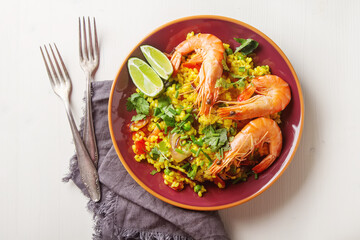 Spanish paella with seafood on a red cloth teralke with lime and fork. Delicious lunch on the shore of the sea shrimp. Light wood background. Top view