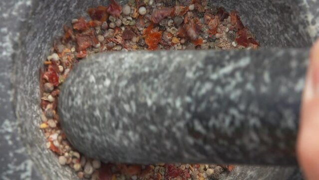 Close-up of heavy pestle grinding spices and peppers in the grey stone mortar