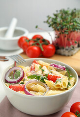 Bowl of delicious pasta with tomatoes, onion and cheese on table, closeup