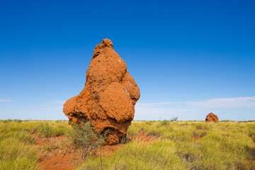 Red Termite mound in arid semi-desert landscape against blue sky
