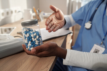 Obraz na płótnie Canvas Hands of young African American male clinician holding jar with white and blue pills while recommending them to patient