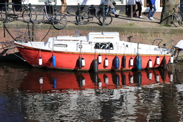 Fototapeta na wymiar Red Boat and People Walking Close Up in Amsterdam, Netherlands