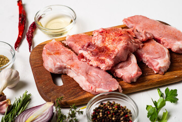 Raw meat steaks on a cutting board. White background. Preparation for cooking pork meat. Various spices, seasonings lie nearby.