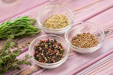 Various spices in glass bowls on a purple wooden background. Black and red pepper, oregano, coriander.