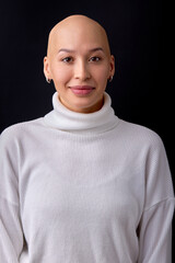 Studio headshot portrait of attractive young bald female with shaved head against black studio background, smiling at camera. Cancer survivor beauty portrait. People, healthcare concept