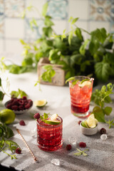 Raspberry cocktail with lime,mint,ice cubes and fresh berries on grey background with juicy summer greenery.Beautiful photo of refreshing drink.