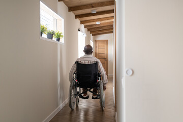 Rear view of young African American man with disability sitting on wheelchair while moving along...
