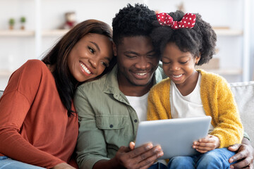 Happy Black Family With Preteen Daughter Relaxing With Digital Tablet At Home