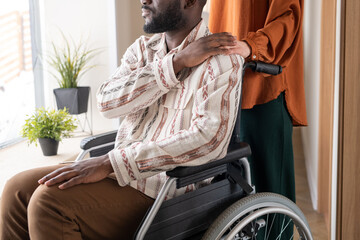 Side view of young African American man with disability keeping his hand on that of Caucasian...