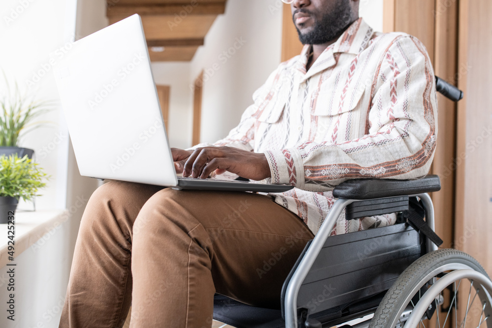 Poster close-up of young man with disability working in the net in home office while sitting in wheelchair 