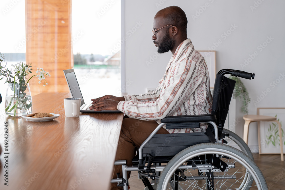 Aufkleber Side view of serious black man working in the net or analyzing online data while sitting in front of laptop by table